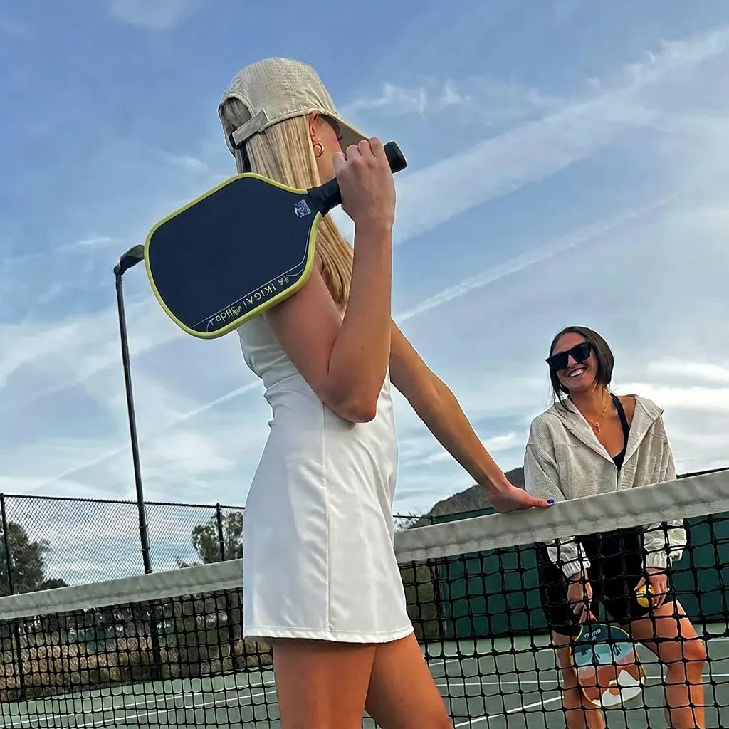 Kaksi naista pickleball-kentällä mailoineen verkolla